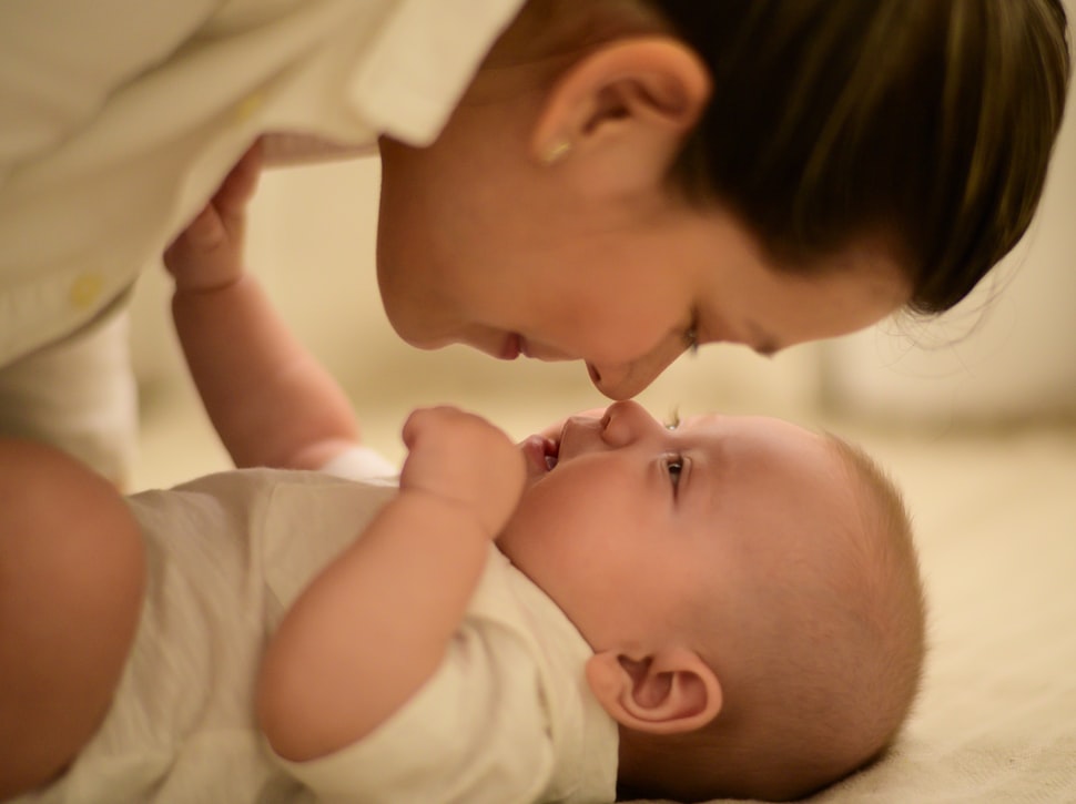 Mother touching noses with her baby while laying on the bed